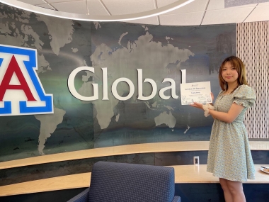 Veronica stands in Global Center lobby holding a certificate for her work with intl admissions