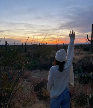 Veronica stands at dusk facing a beautiful Tucson sunset, raising her right arm to the sky