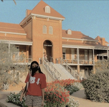 Ananya is standing in front of Old Main. She is wearing a red Bear Down icon t-shirt.