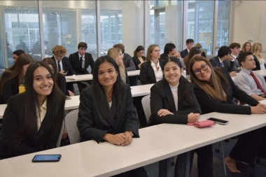 Ananya is seated in the front row, second from left, in a classroom with a large group of students dressed in business attire.